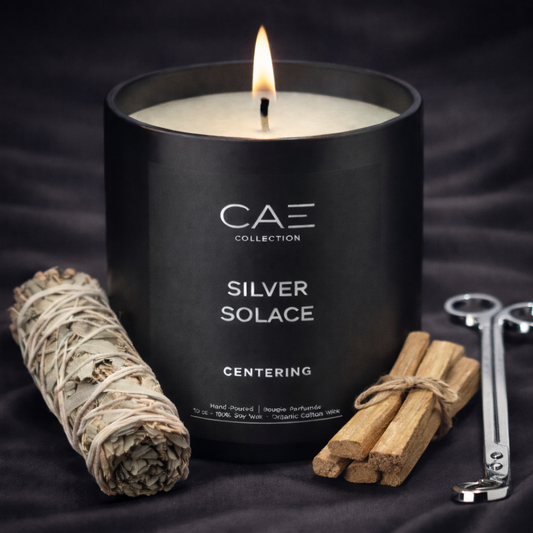 Black candle labeled 'Silver Solace' with Palo Santo and Smoked Oud with a silver candle trimmer on a dark background